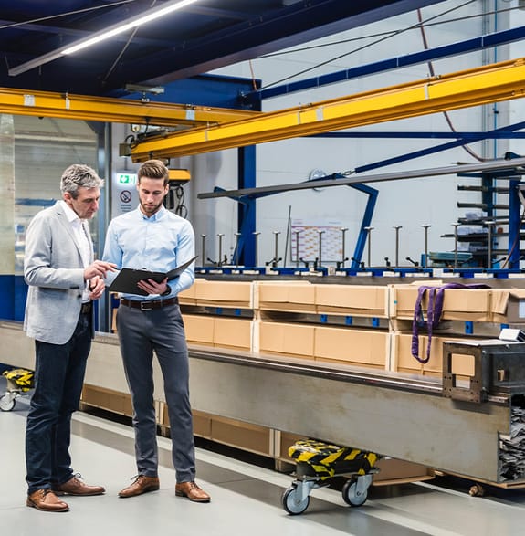 Two men discuss business plans next to a machine in a factory
