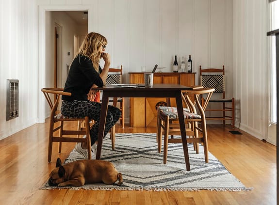 Woman sitting at a table in her house with dog at her feet
