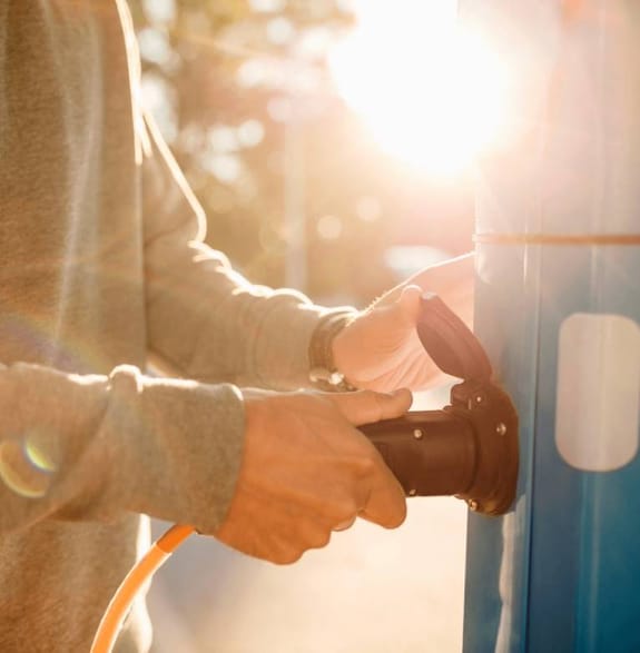 A man plugs an electric car charger into a charging unit