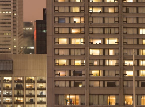 Close up of multiple flat windows across multiple buildings in a city at dusk