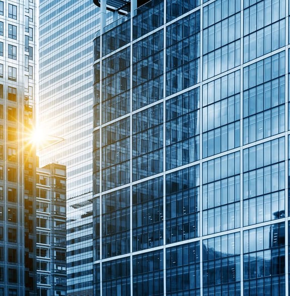 Looking into a corporate skyscraper while the sun breaks past the building next to it