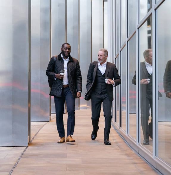 Two men talking as they walk along a corporate office with coffees