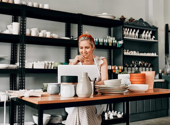 Woman sitting alone and using her laptop in her pottery workshop