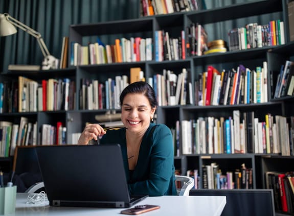 A lady laughs while listening to a webinar in her library