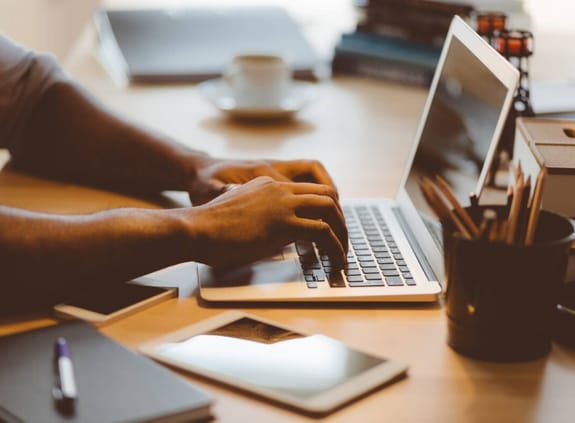 A man types at a laptop surrounded by stationery