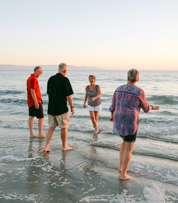 Two middle-ages couples laugh in the breaking waves by the beach