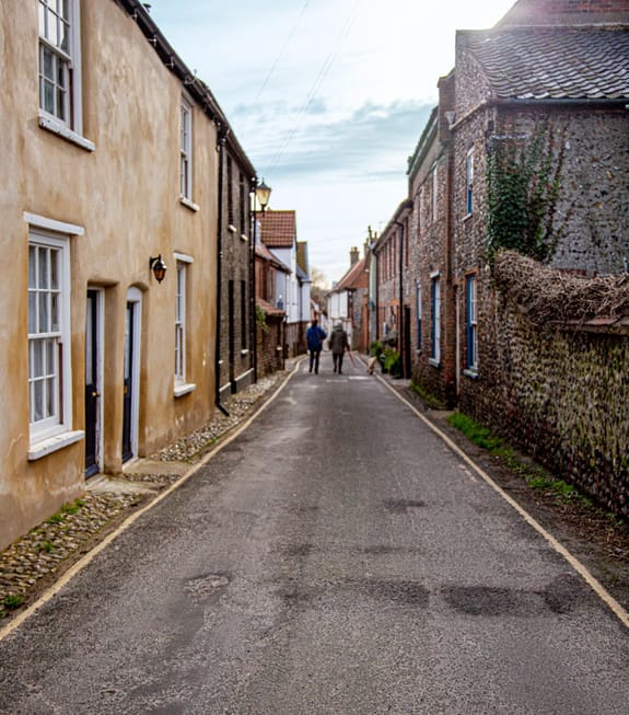 A couple with a dog walk down a narrow British town street