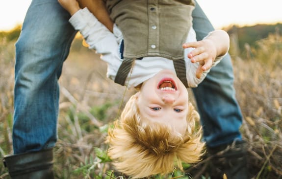A young boy laughs while being held upside down