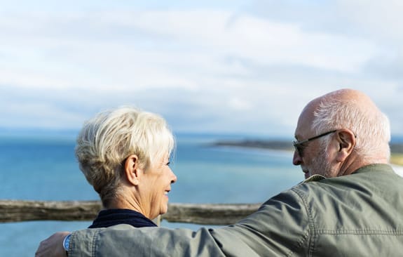 Elderly couple smile at each other overlooking the ocean
