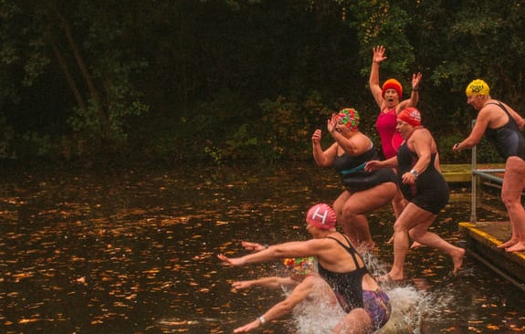 Group of older women in swimming kits bravely jumping into a cold autumn pond