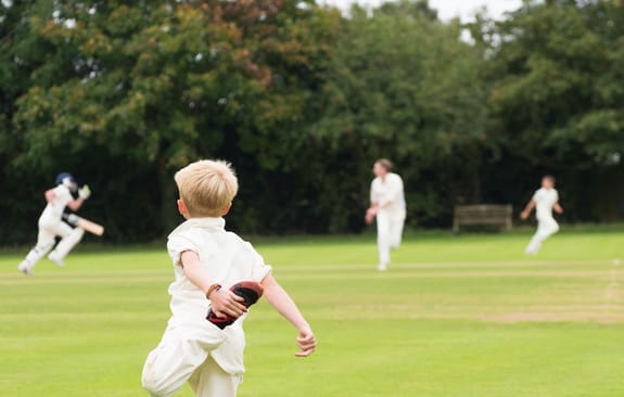 Child in cricket whites stretching in the outfield during a match