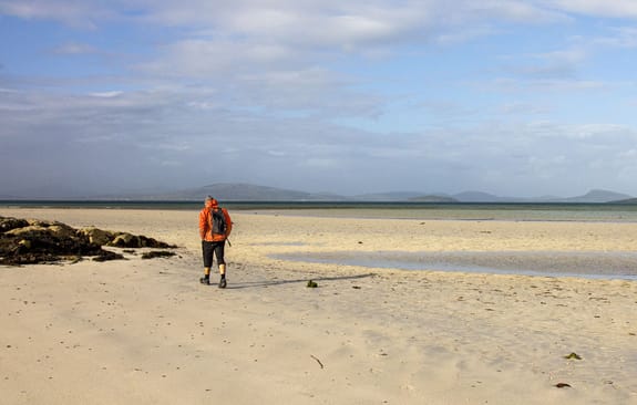 Landscape of a person in an orange jacket walking on an empty beach