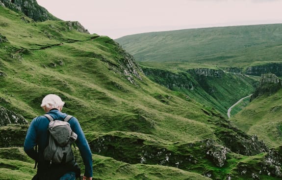 Grey-haired man with backpack ascends a rocky hill
