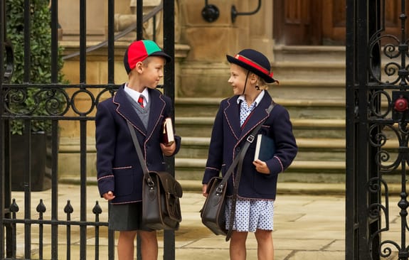 Two children in school uniform wait outside a gate