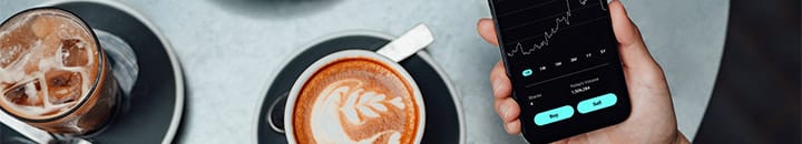 Person checking investment on mobile while drinking coffee