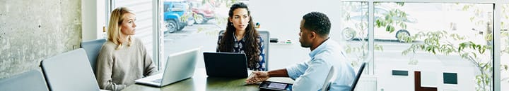 Three people discussing business around a meeting table