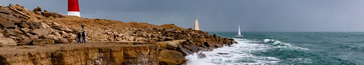 Lighthouse standing on tops of rocks with waves crashing into them