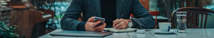Male checking his finance app on his phone and making notes