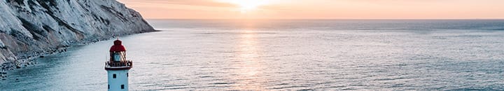 Lighthouse with cliff face and sun setting in background