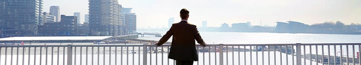Business man standing on bridge looking out over river