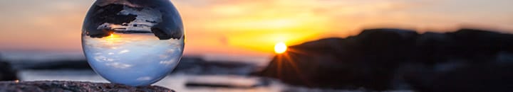 Cystal ball sitting on top of a rock by the sea with sunset