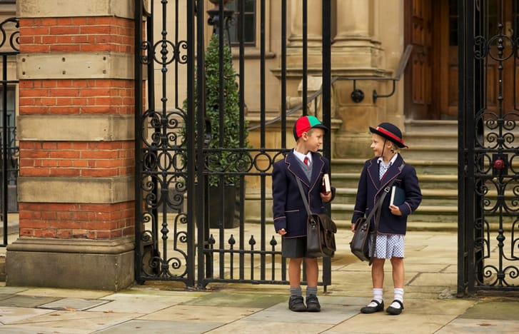 Two children in school uniform wait outside a gate