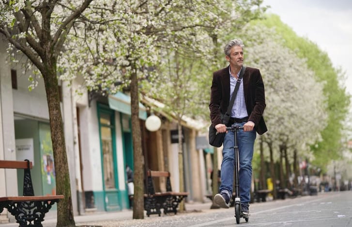 Middle-aged man scoots down a tree-lined street