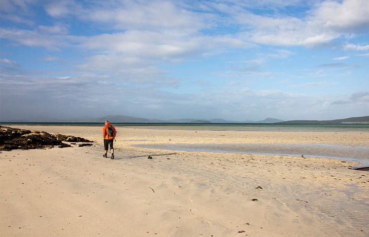 Person in orange jacket walks on an empty beach