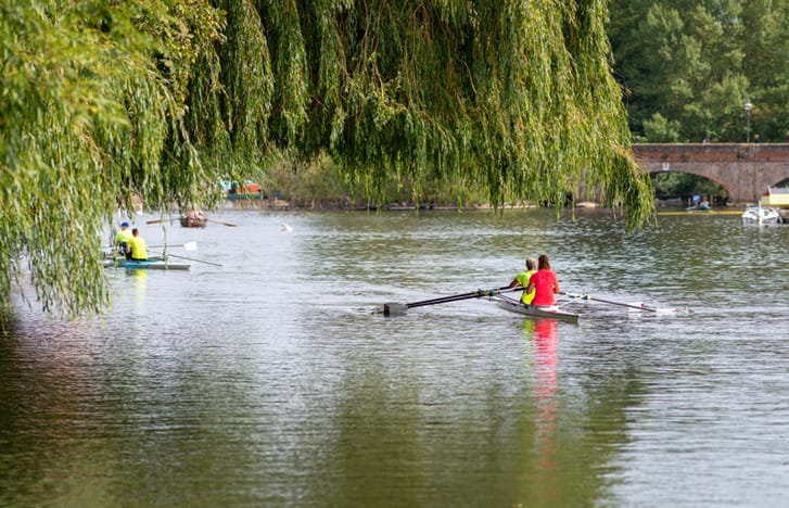 People in fluorescent kits rowing double sculls down a river