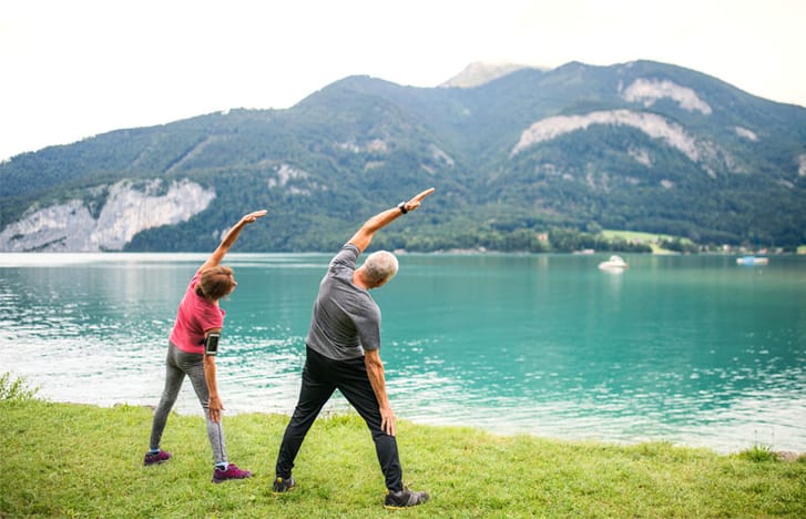 A couple stretching together beside a lake