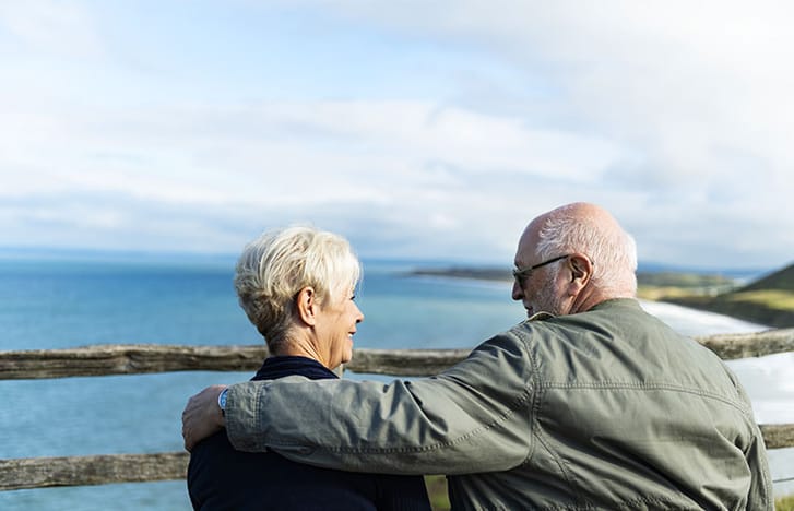 Elderly couple smiling at each other on a windy coastal lookout