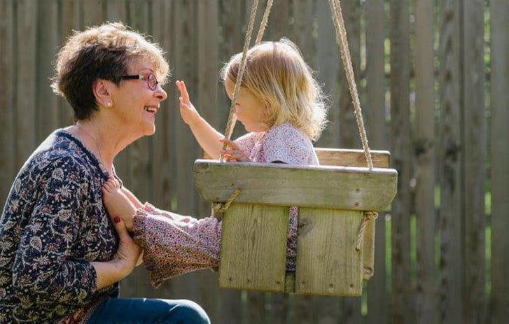 Middle aged female playing grand daughter in swing