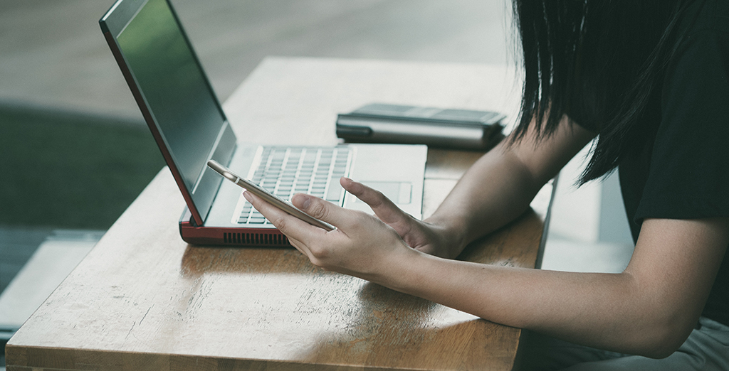 Young female accessing mobile phone next to her laptop