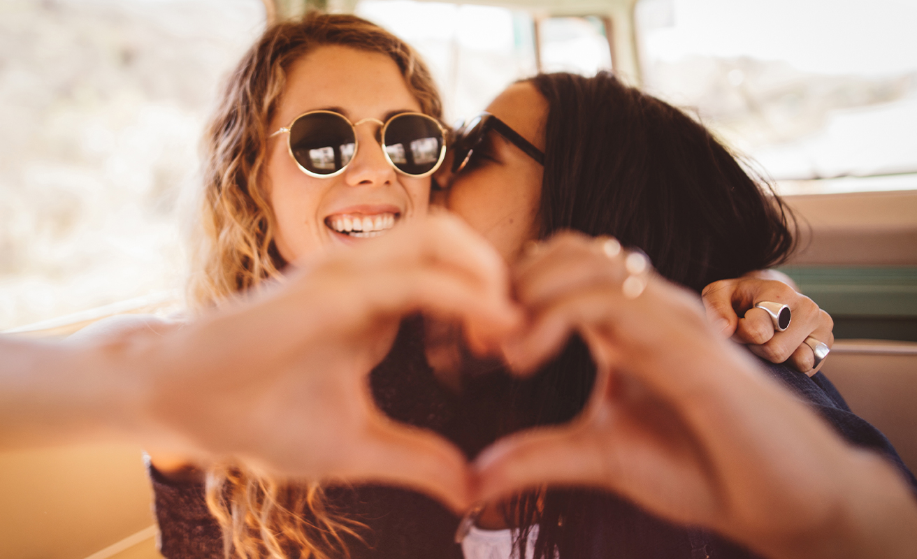 Female friends making heart with their hands in their van