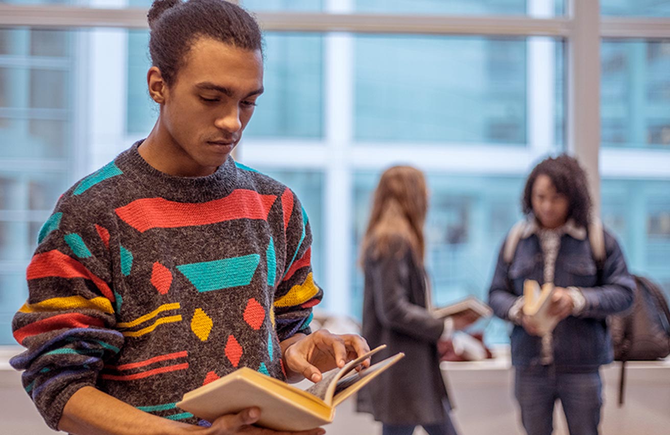 Young male student reading a book in corridor