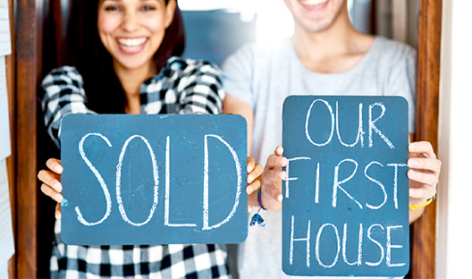 Young couple holding signs saying Sold Our First House