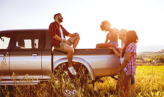 Friends sitting on their truck in the middle of a field