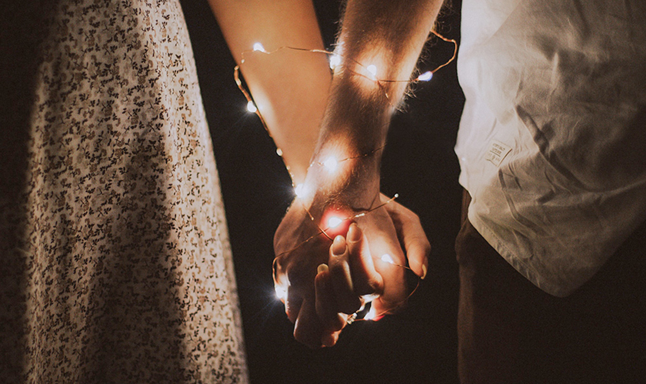 Couple holding hands with lights wrapped around their arms