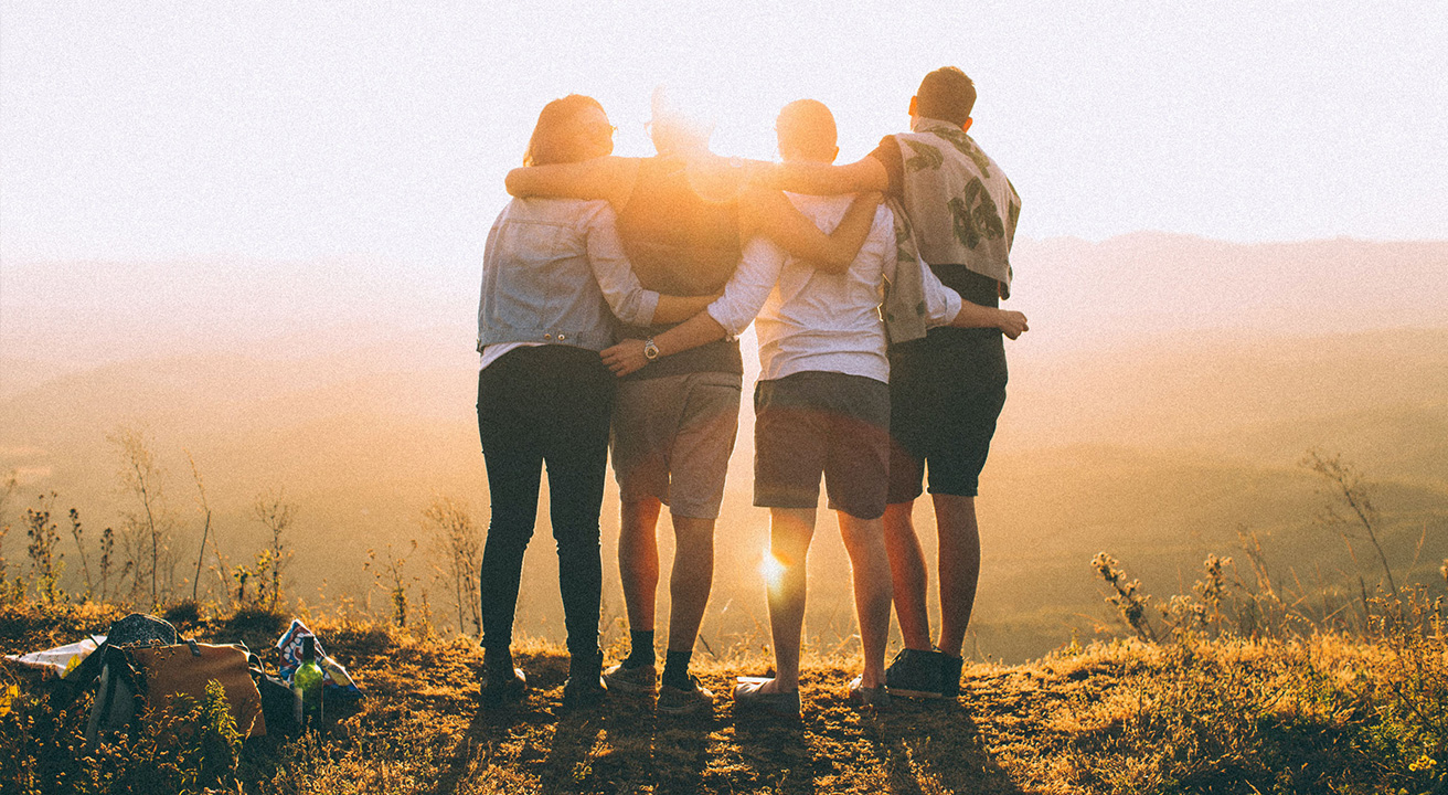 Friends locked arms looking into sunset from behind