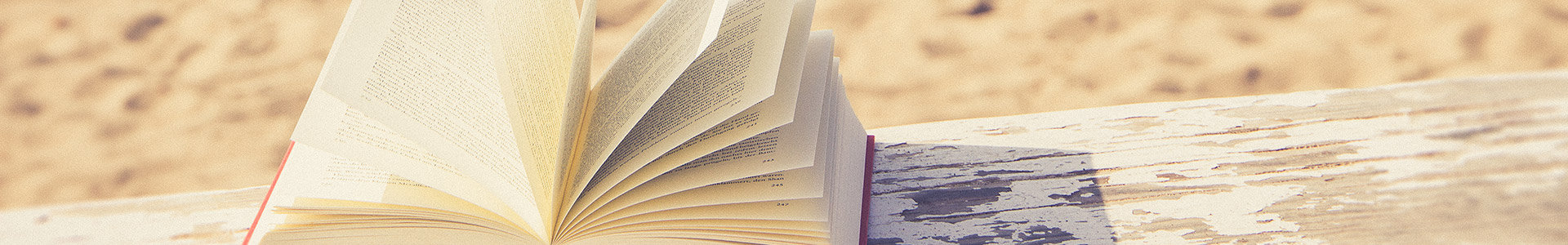 Open book on wooden bench next to beach