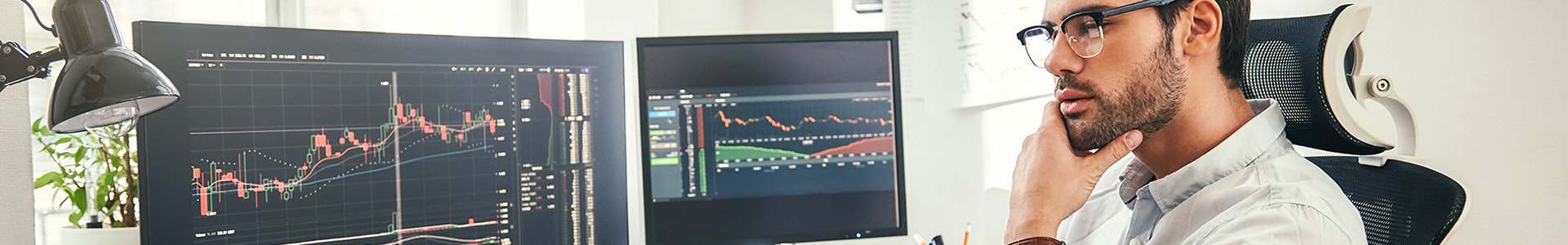 Investor looking at markets on two computer screens