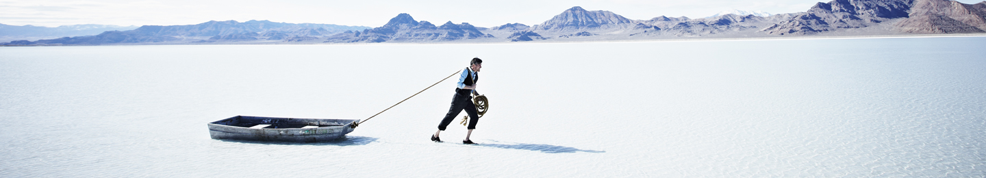 Businessman dragging boat behind him in shallow water