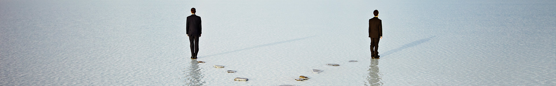 Two men walking on stepping stones in opposite directions