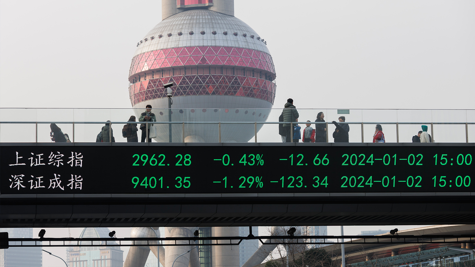 People walk on a pedestrian bridge displaying the Shanghai and Shenzhen stock indexes