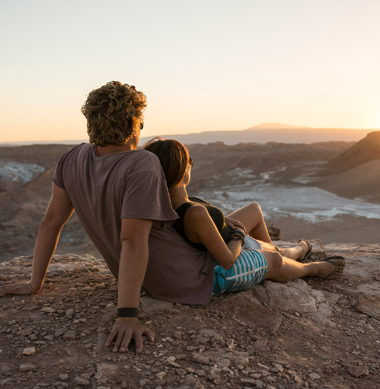 Young couple sitting on a cliff top watching the sunset