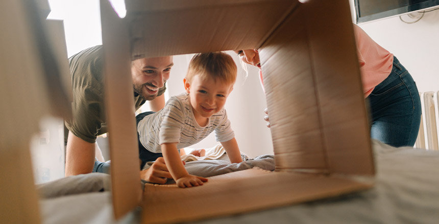 Child looking into a box on the floor with parents at the side