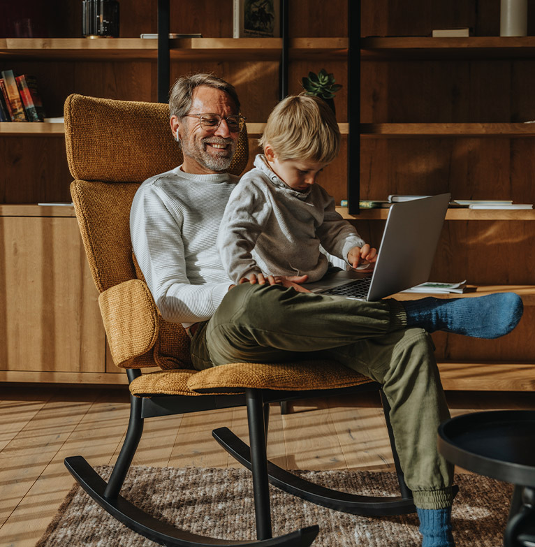 Older male sitting in a rocking chair with his grandson looking at a laptop