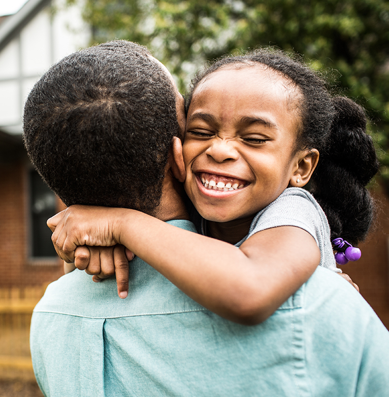A young girl with a smile hugging an adult in their new home, showing happiness after receiving a home loan.