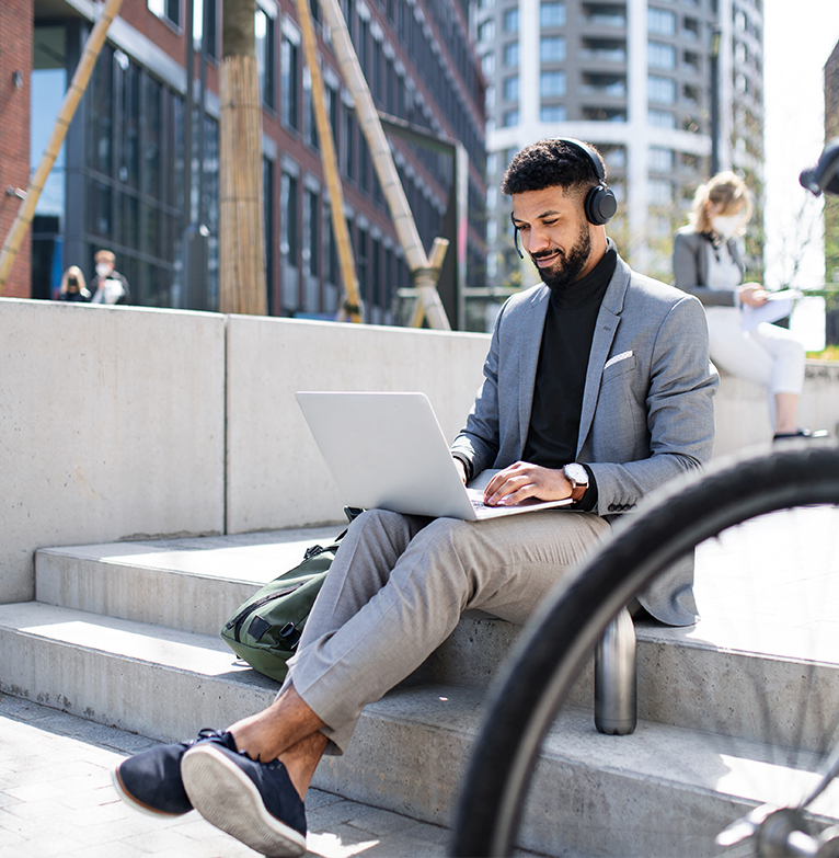 Business man sitting on his laptop working on his digital investment platform on a step outdoors with a bicycle next to him 