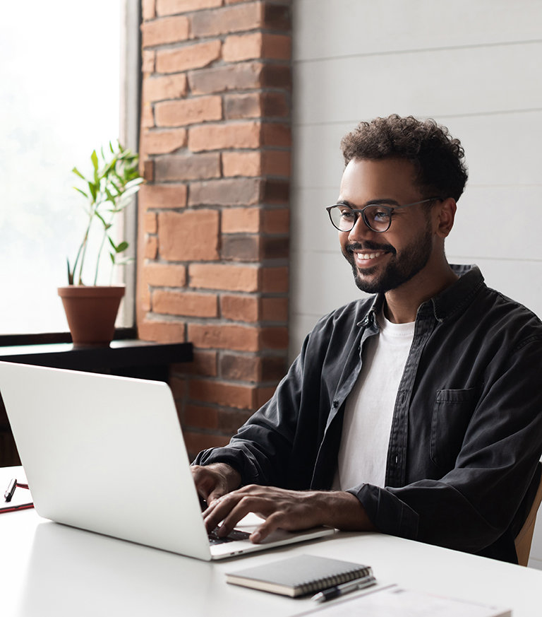 A man with glasses engages in online share trading on a laptop at his desk